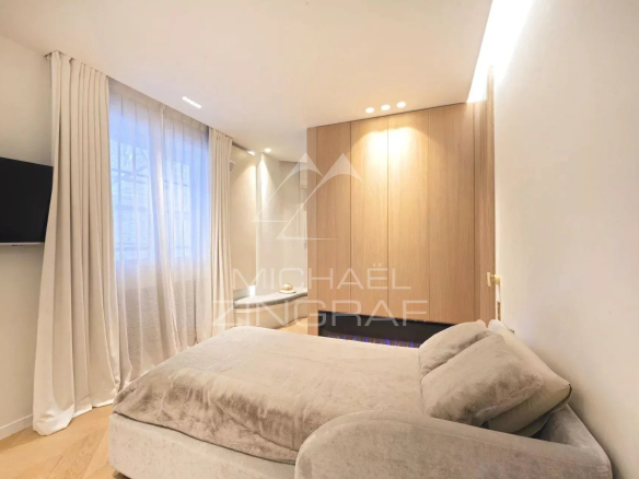 Modern apartment bedroom with bed and wall-mounted TV, soft lighting.