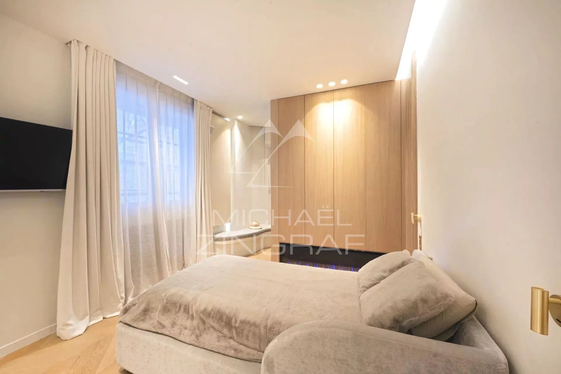 Apartment room in Paris 7th arrondissement Modern apartment bedroom with bed and wall-mounted TV, soft lighting.