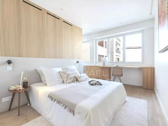 Chambre d'un appartement rénové à Paris, avec un lit, un bureau et des fenêtres lumineuses.