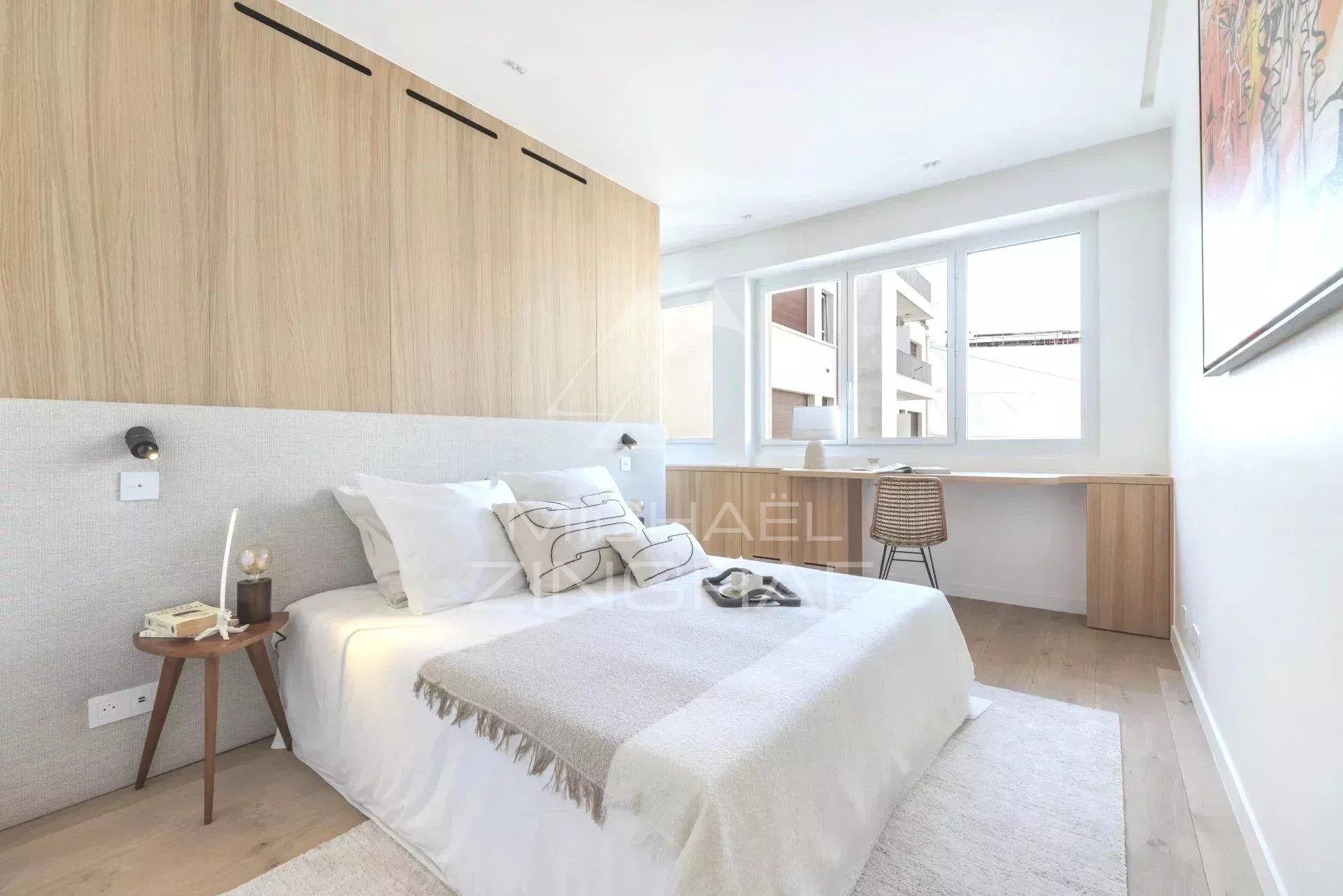 Chambre d'un appartement rénové à Paris, avec un lit, un bureau et des fenêtres lumineuses.