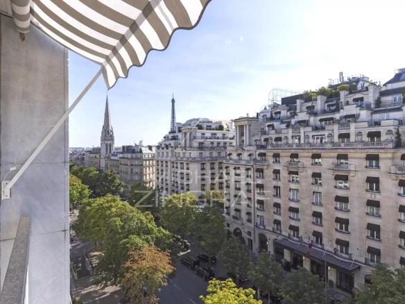 Vue depuis un balcon d'un appartement sur l'Avenue George V à Paris, montrant des bâtiments haussmanniens et la tour Eiffel au loin.