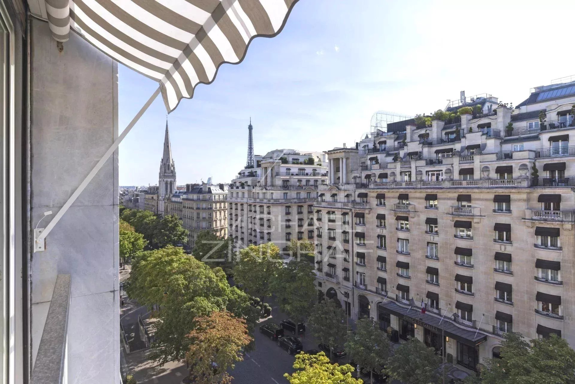 Vue depuis un balcon d'un appartement sur l'Avenue George V à Paris, montrant des bâtiments haussmanniens et la tour Eiffel au loin.