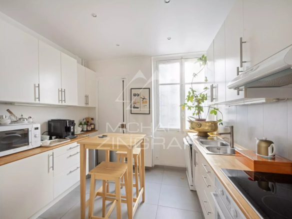Cuisine moderne et lumineuse d'un appartement à Paris 7, avec meubles blancs et plan de travail en bois.