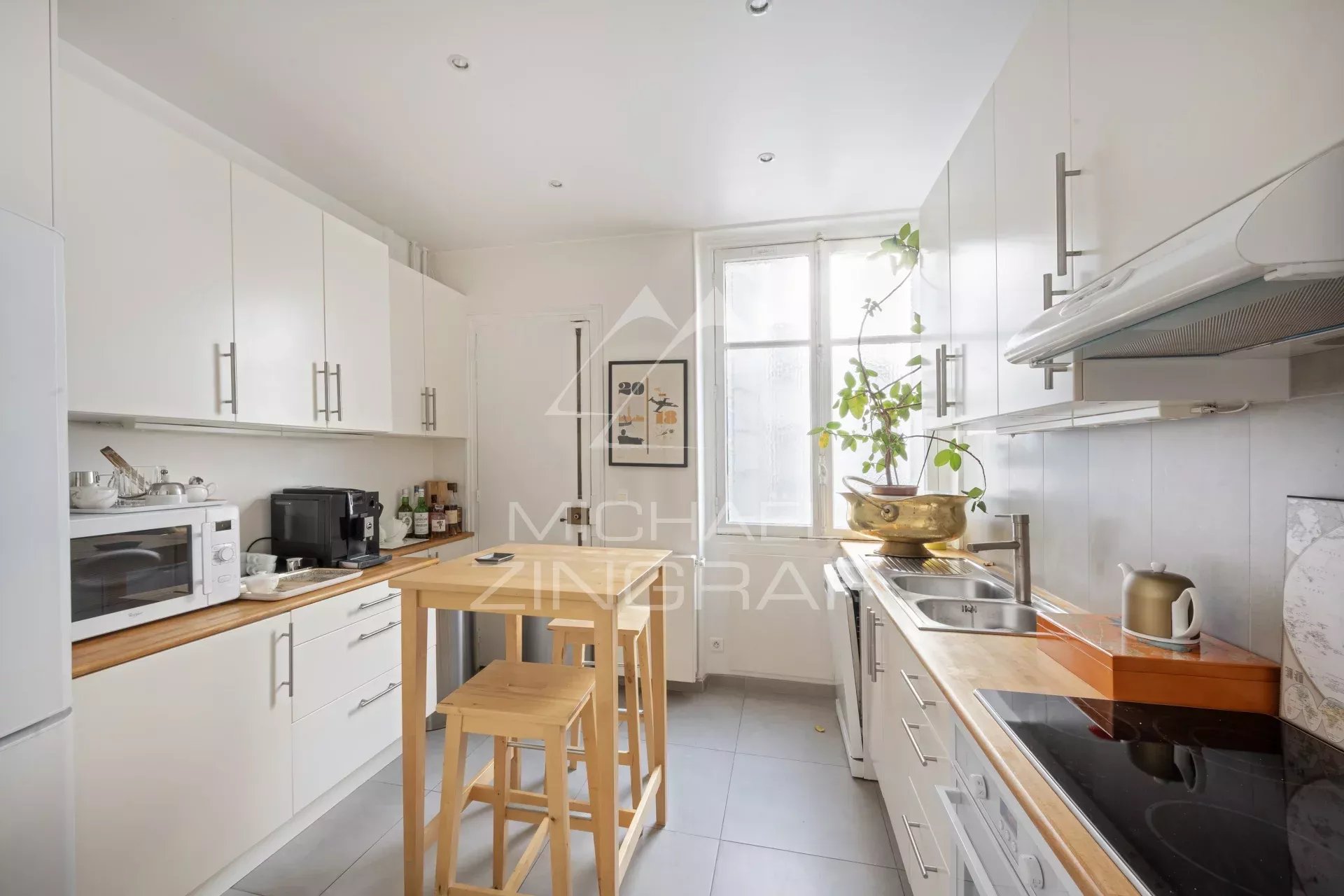 Cuisine moderne et lumineuse d'un appartement à Paris 7, avec meubles blancs et plan de travail en bois.