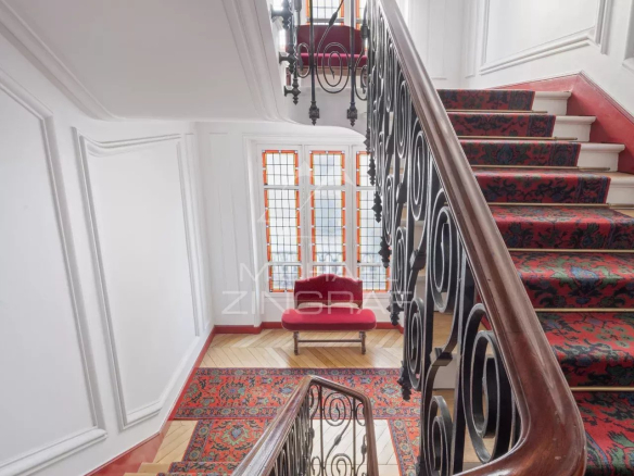 Escalier avec rampe en fer forgé et tapis dans un immeuble à Paris 7ème.