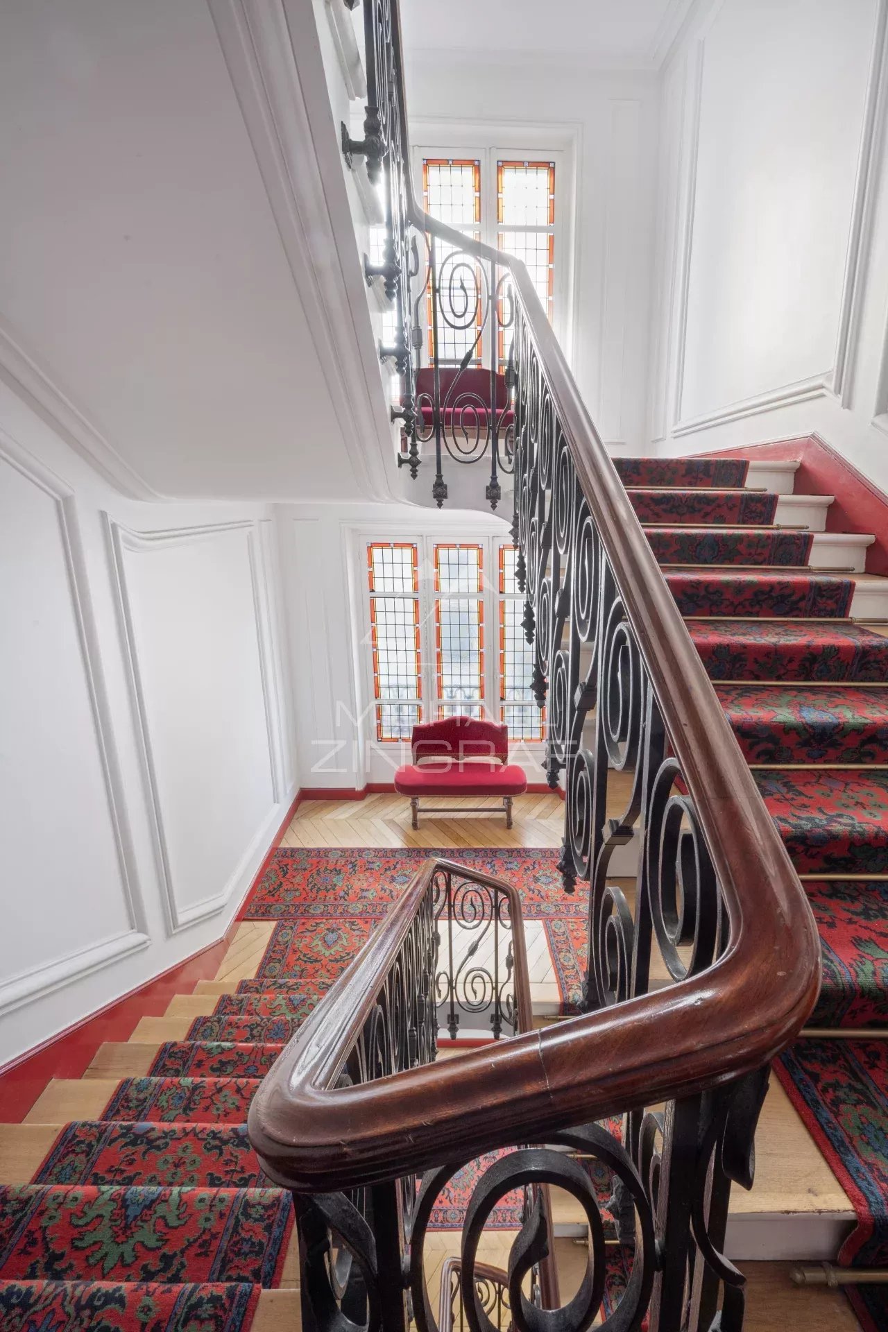 Escalier avec rampe en fer forgé et tapis dans un immeuble à Paris 7ème.