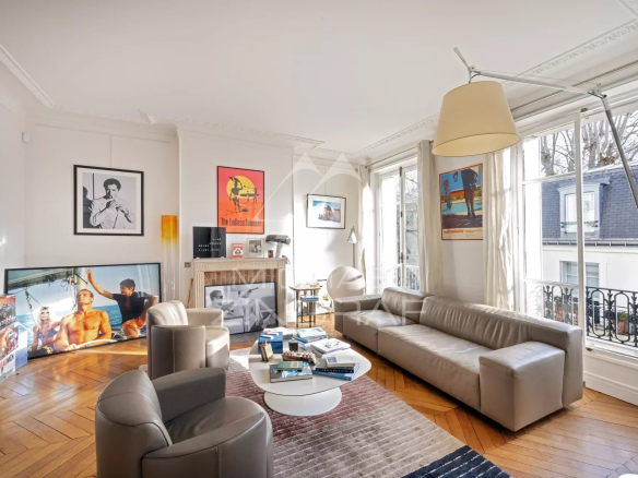 Salon lumineux d'un appartement de 115 m2 à Paris, avec canapé, cheminée et œuvres d'art aux murs.