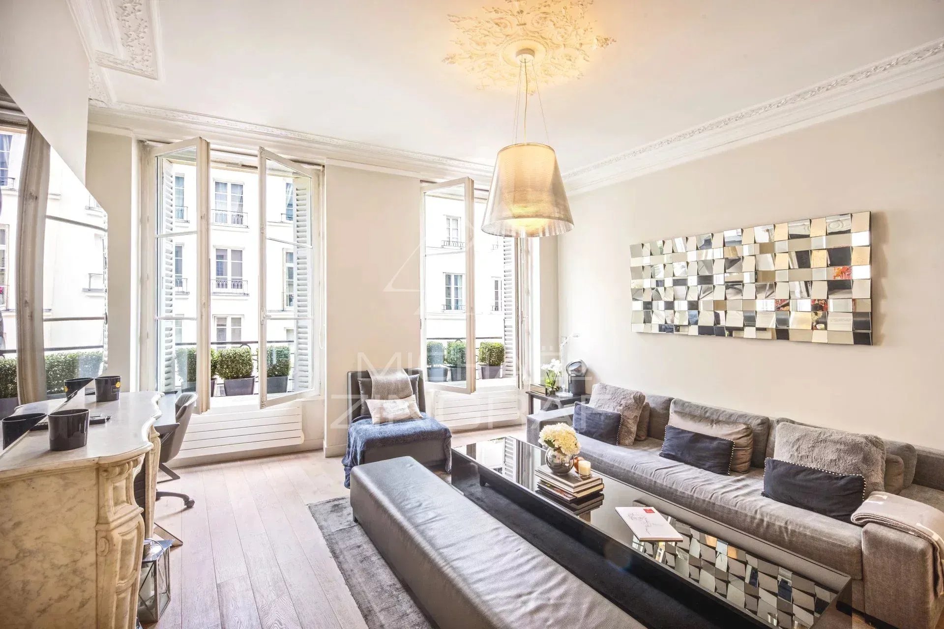 Salon lumineux avec canapé et table basse, fenêtres ouvertes sur cour, décor moderne.