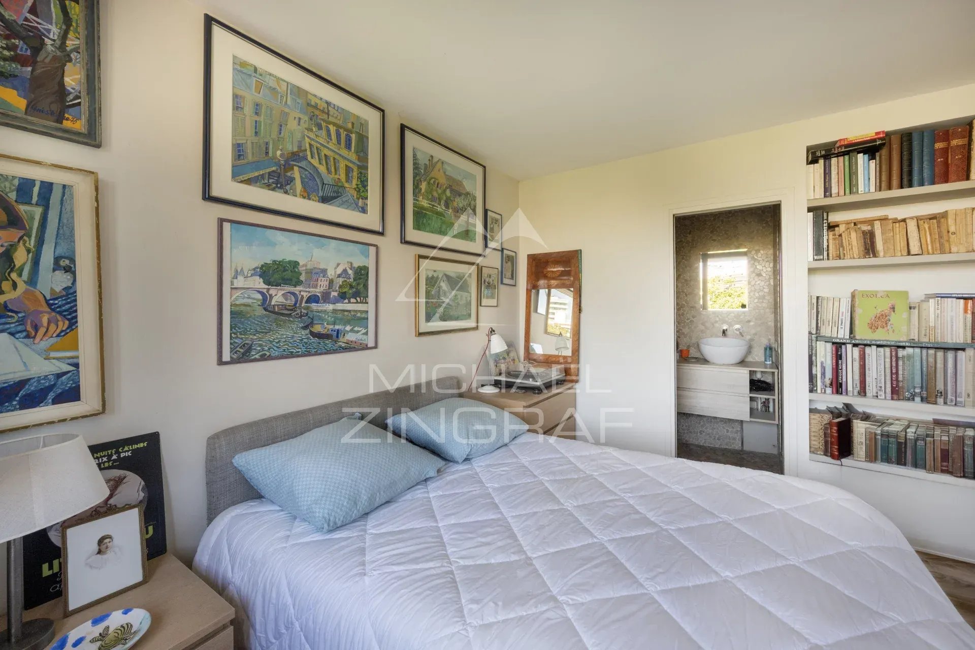 Chambre d'un penthouse à Paris avec lit, bibliothèque et œuvres d'art au mur.