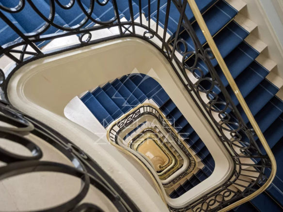 Escalier en colimaçon avec rampe en fer forgé et marches bleues dans un immeuble parisien.