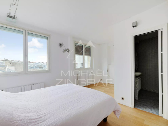 Chambre d'appartement moderne avec vue sur Paris, fenêtre et salle de bain attenante.