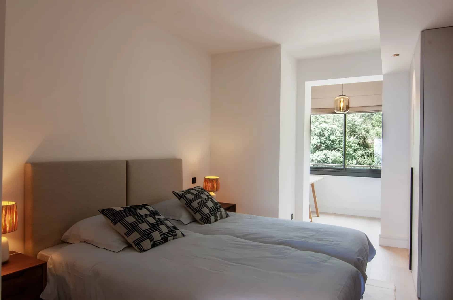 Double room with twin beds and windows overlooking a green outdoor space.
