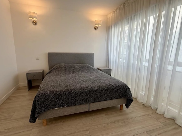 Chambre d'un appartement lumineux avec lit double et rideaux blancs.