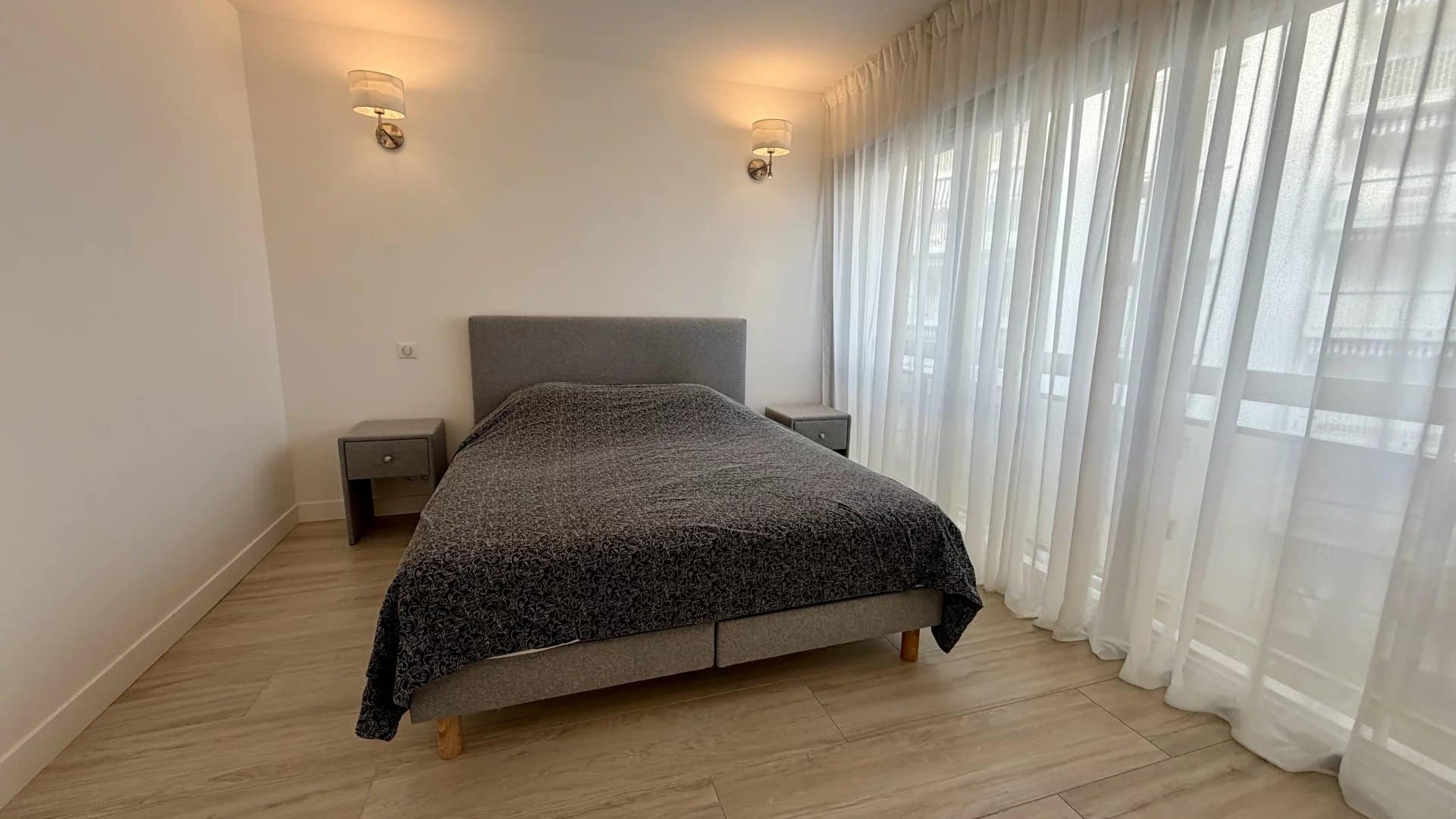 Chambre d'un appartement lumineux avec lit double et rideaux blancs.