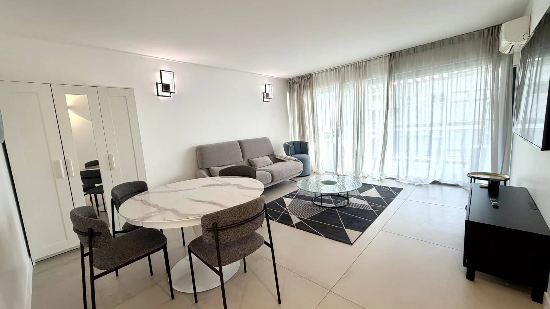 Salon lumineux d'un appartement de 3 pièces à Cannes, avec un canapé, une table et des grandes fenêtres.