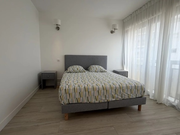 Room in a bright apartment with a double bed and sheer curtains.