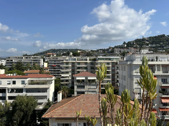 View from a rooftop terrace in Cannes, showing buildings and hills under a cloudy sky.