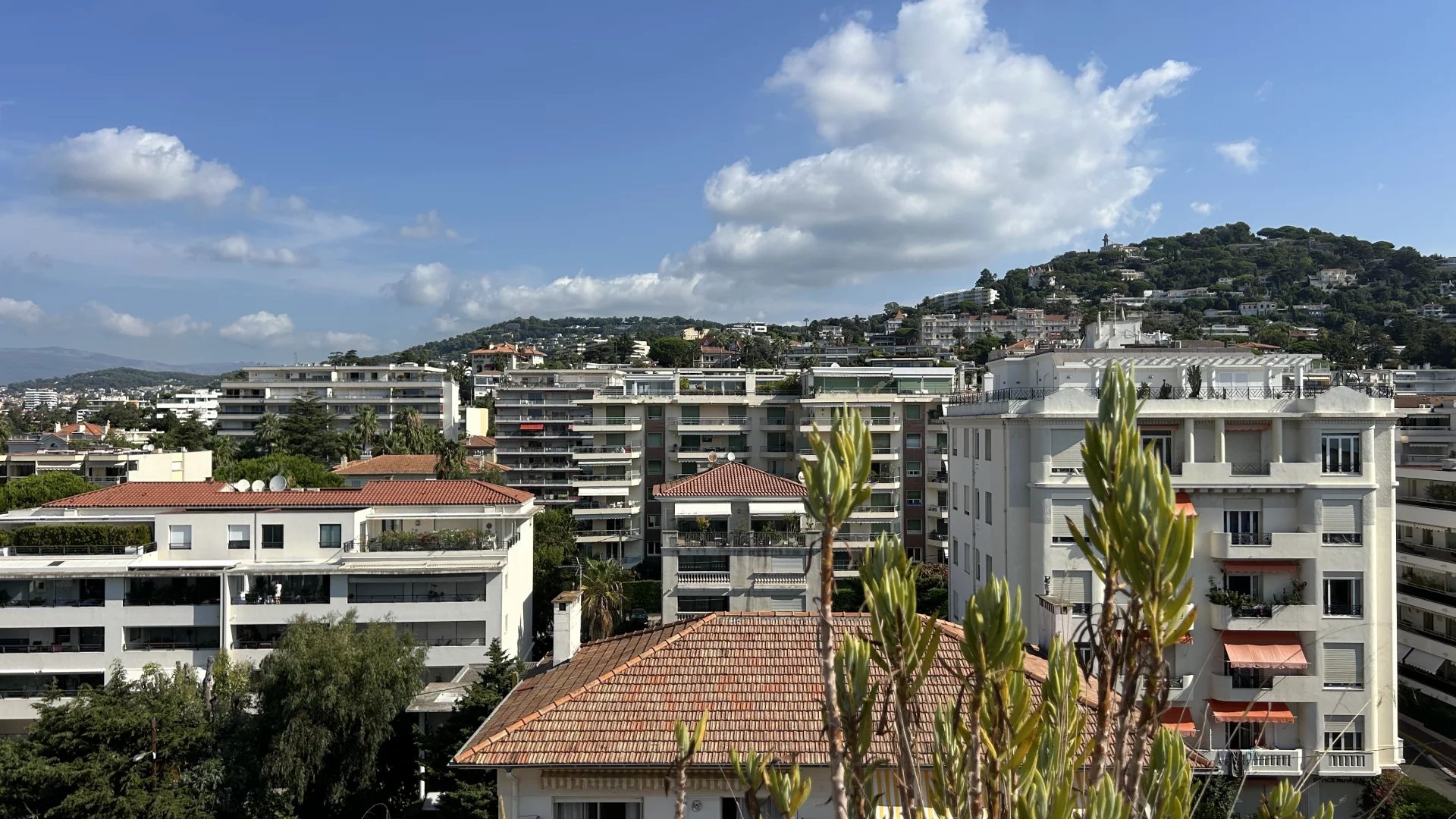 View from the rooftop terrace in Cannes View from a rooftop terrace in Cannes, showing buildings and hills under a cloudy sky.