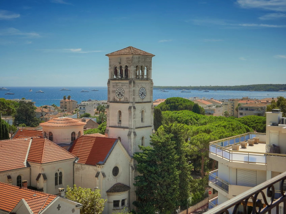 Vue panoramique sur la mer depuis une terrasse à Cannes, avec des bâtiments et une église au premier plan.