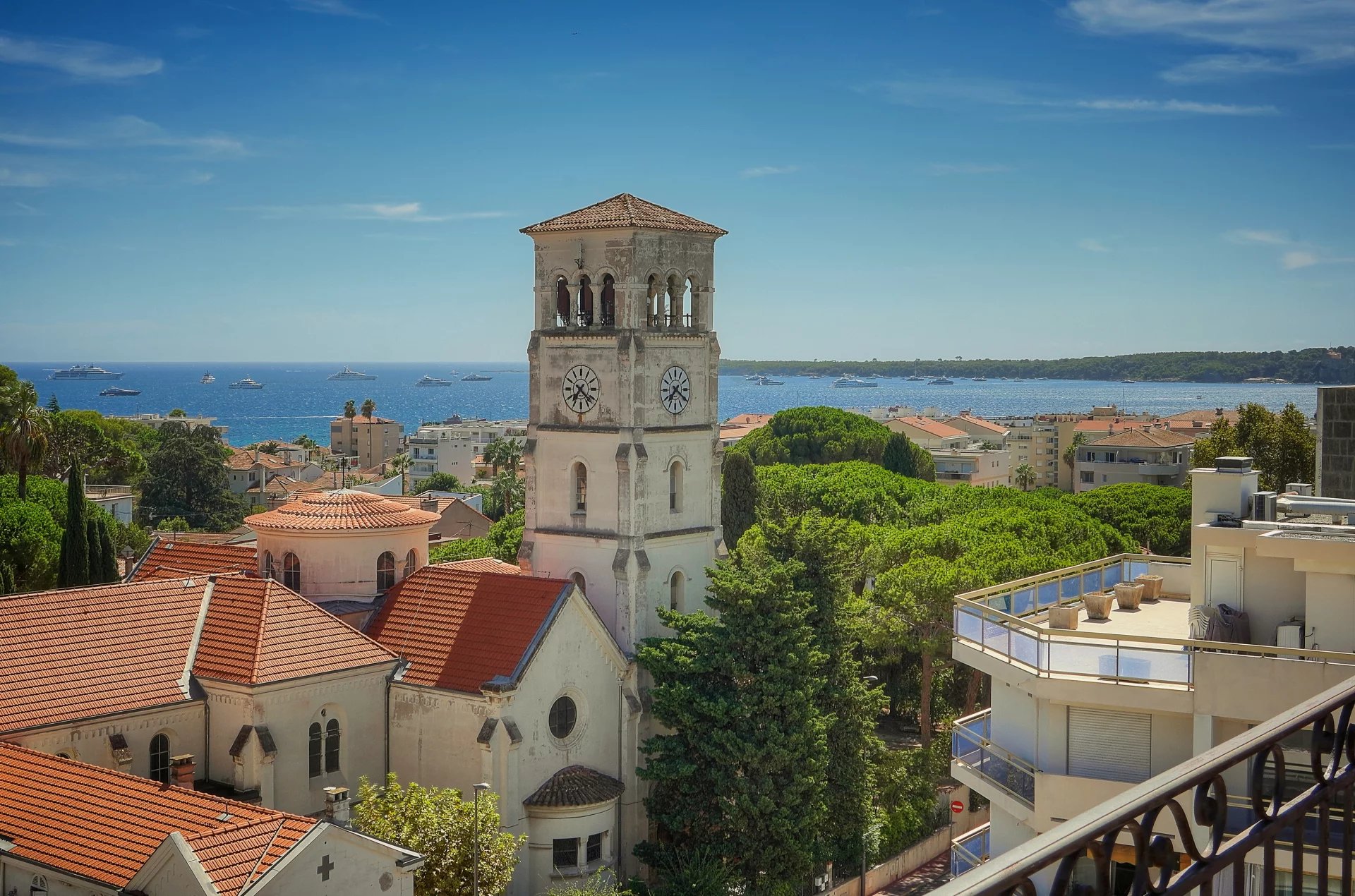 Vue panoramique sur la mer depuis une terrasse à Cannes, avec des bâtiments et une église au premier plan.