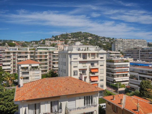Vue panoramique depuis une terrasse d'appartement à Cannes, montrant des bâtiments et la mer au loin.
