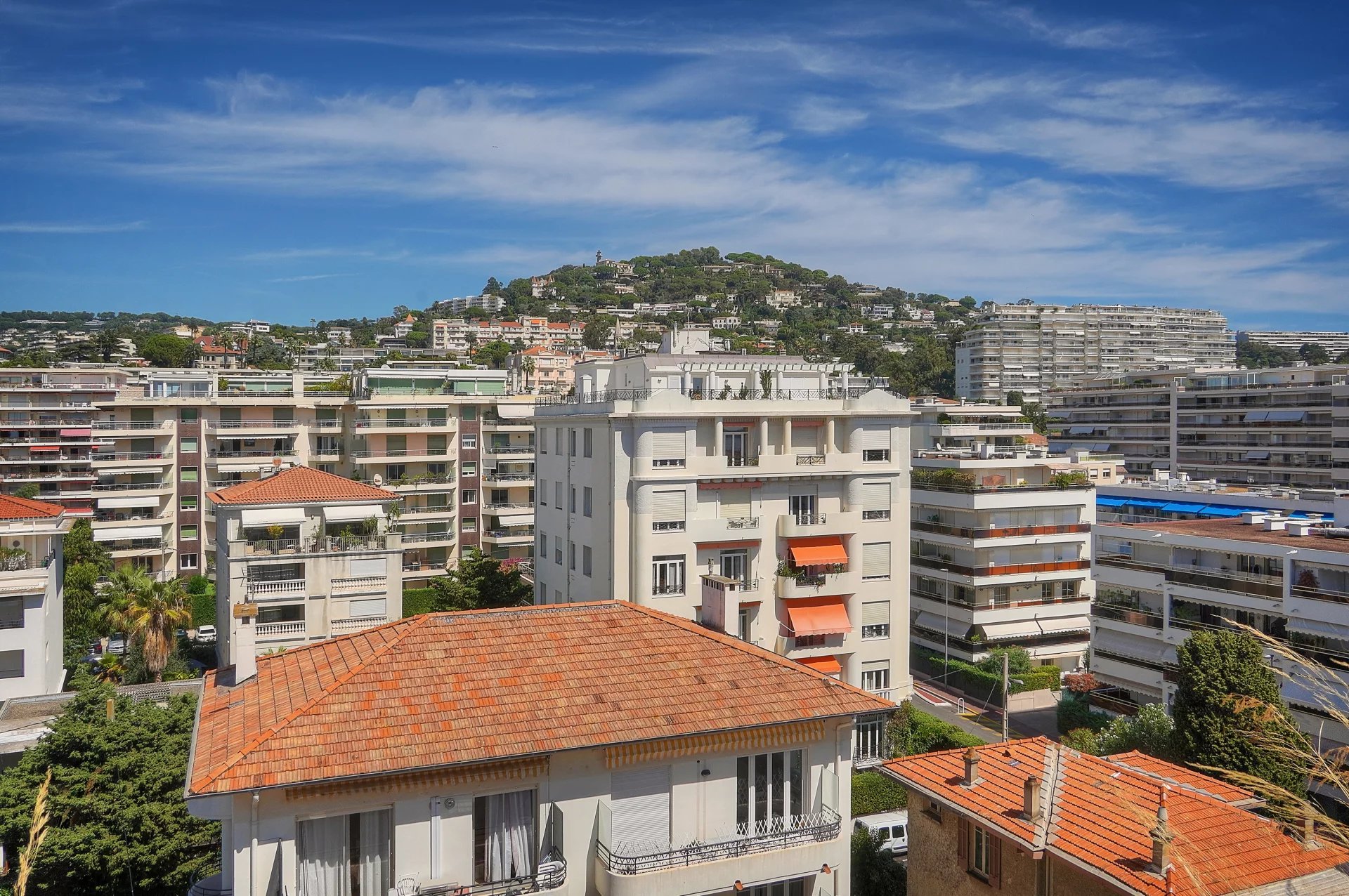 Vue panoramique depuis une terrasse d'appartement à Cannes, montrant des bâtiments et la mer au loin.