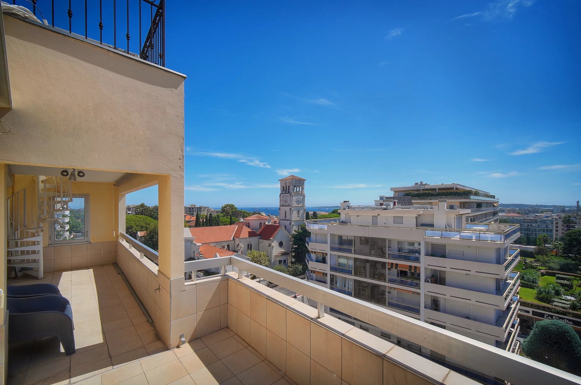 Vue depuis une terrasse d'appartement à Cannes, avec mer en arrière-plan et bâtiments environnants.