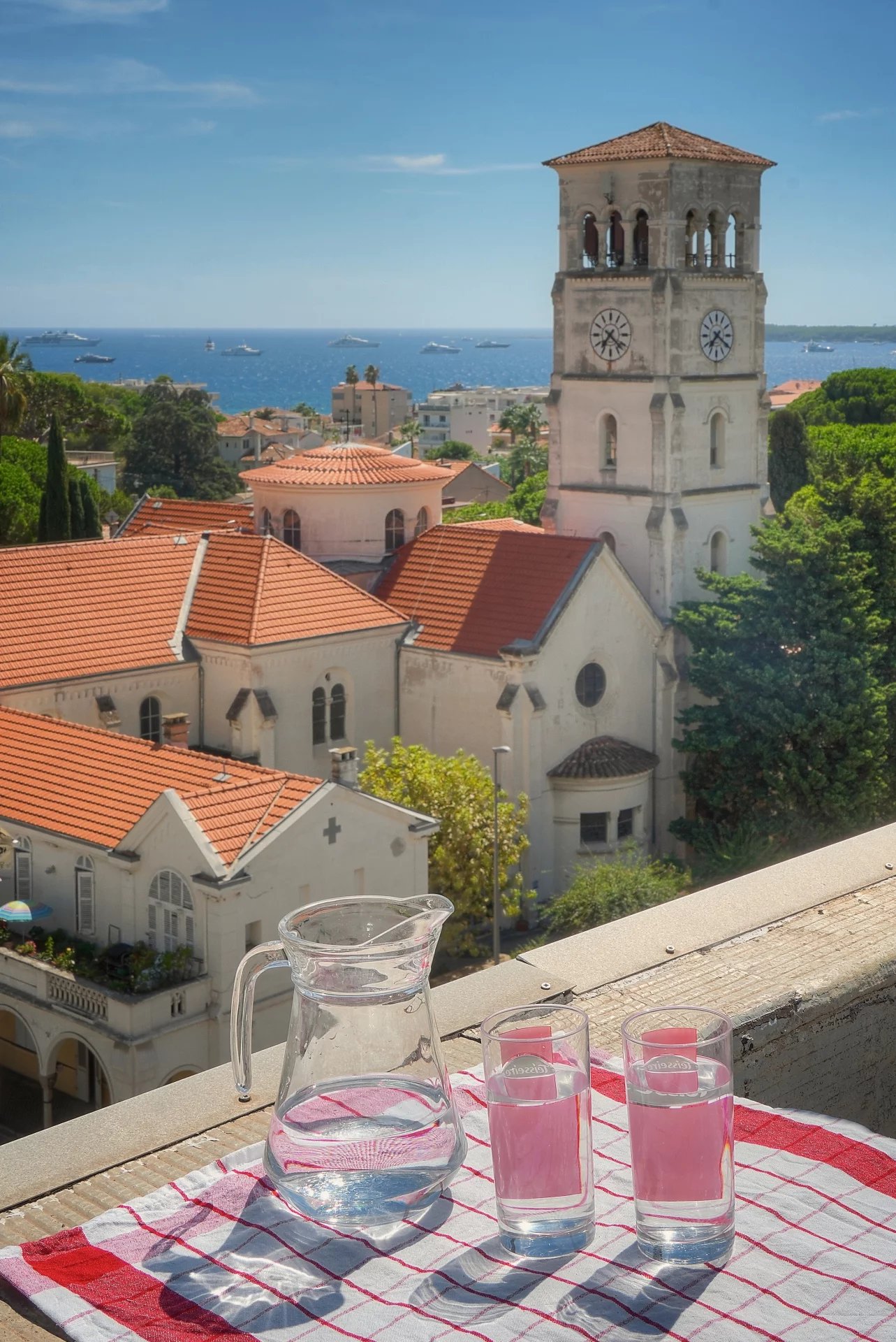 Vue depuis une terrasse avec un pichet et des verres, surplombant des maisons et la mer à Cannes.