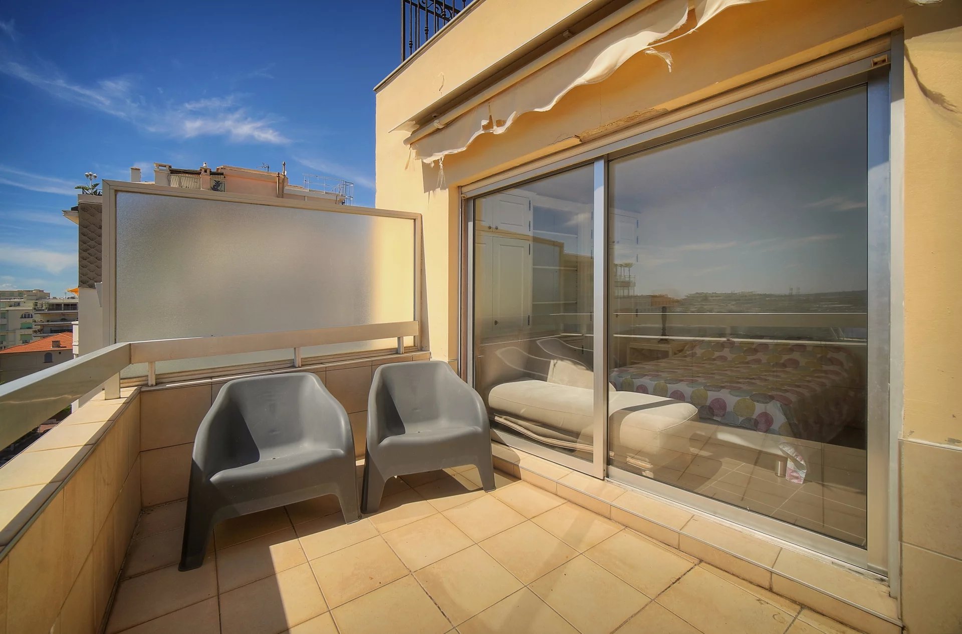 Terrasse d'un appartement à Cannes avec vue sur la mer, deux chaises en plastique sur le balcon.