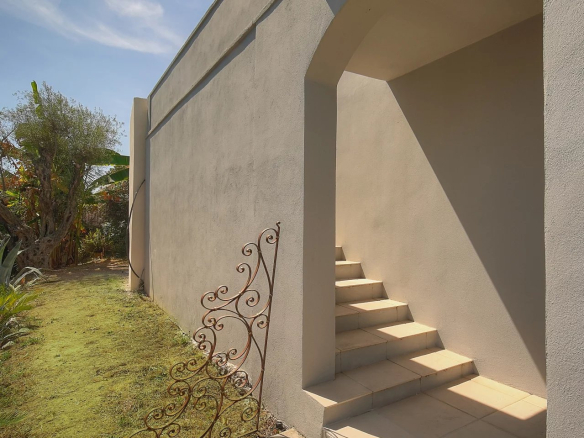 Escalier menant à l'entrée d'une villa à Vence, avec un mur gris et un jardin à côté.