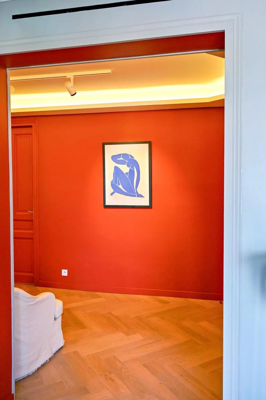 Intérieur d'un appartement bourgeois à Cannes avec un mur rouge et une œuvre d'art moderne.