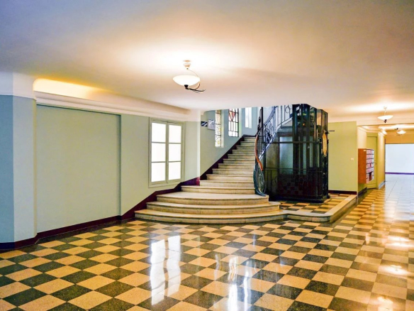 Hall d'entrée spacieux d'un immeuble bourgeois avec escalier et sol en carrelage à motifs.