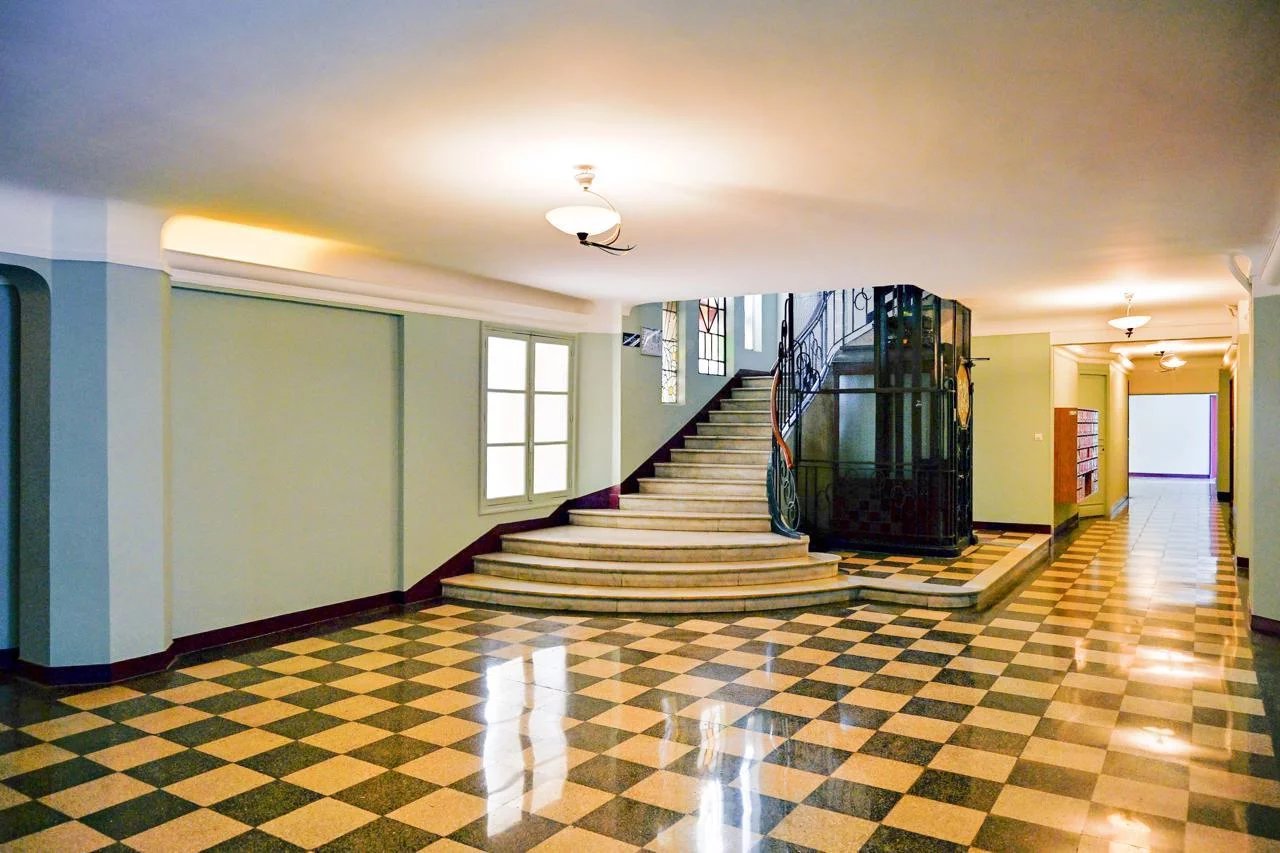 Hall d'entrée spacieux d'un immeuble bourgeois avec escalier et sol en carrelage à motifs.