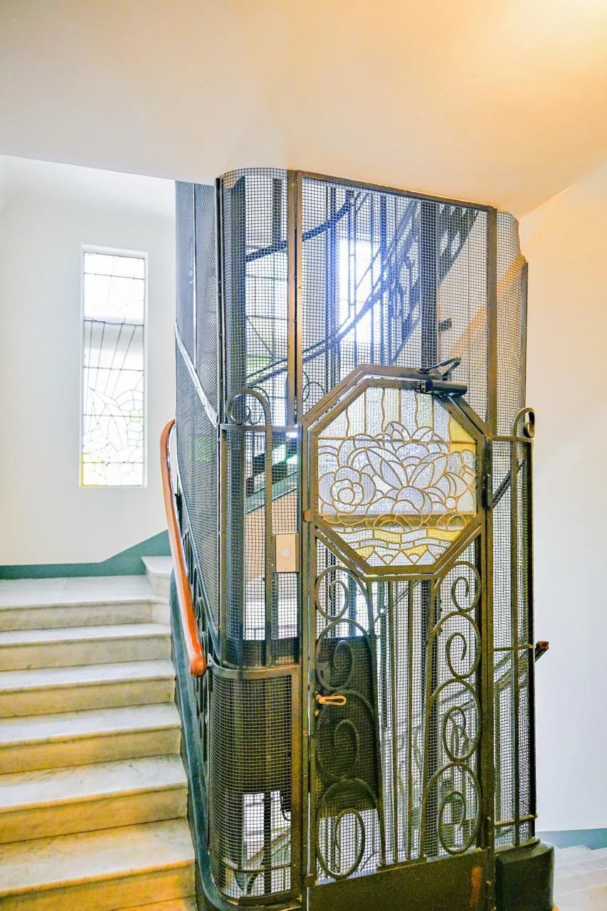 Escalier d'une résidence bourgeoise à Cannes avec une porte en fer forgé et des fenêtres en vitraux.
