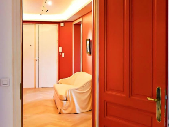 Vue d'un hall d'entrée avec une porte rouge et un salon lumineux en arrière-plan.
