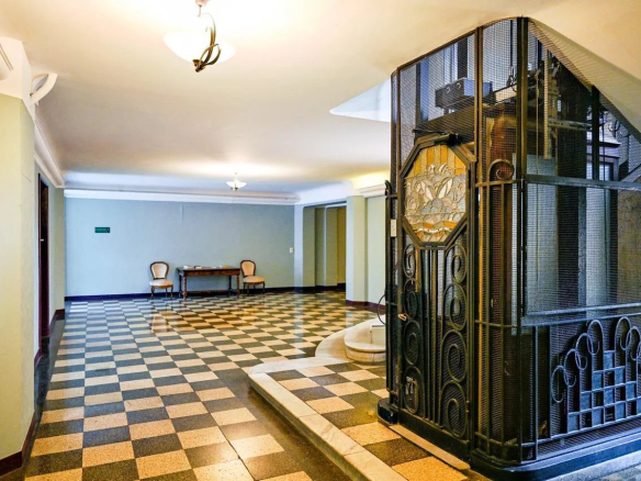 Hall d'entrée d'un appartement bourgeois avec un ascenseur en fer forgé et un sol en carreaux à motifs.