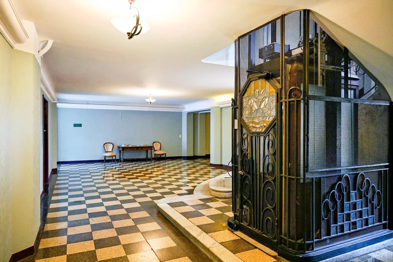 Hall d'entrée d'un appartement bourgeois avec un ascenseur en fer forgé et un sol en carreaux à motifs.