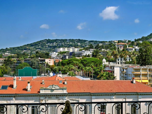 Vue depuis un balcon sur des bâtiments et des collines à Cannes, avec ciel bleu et nuages.