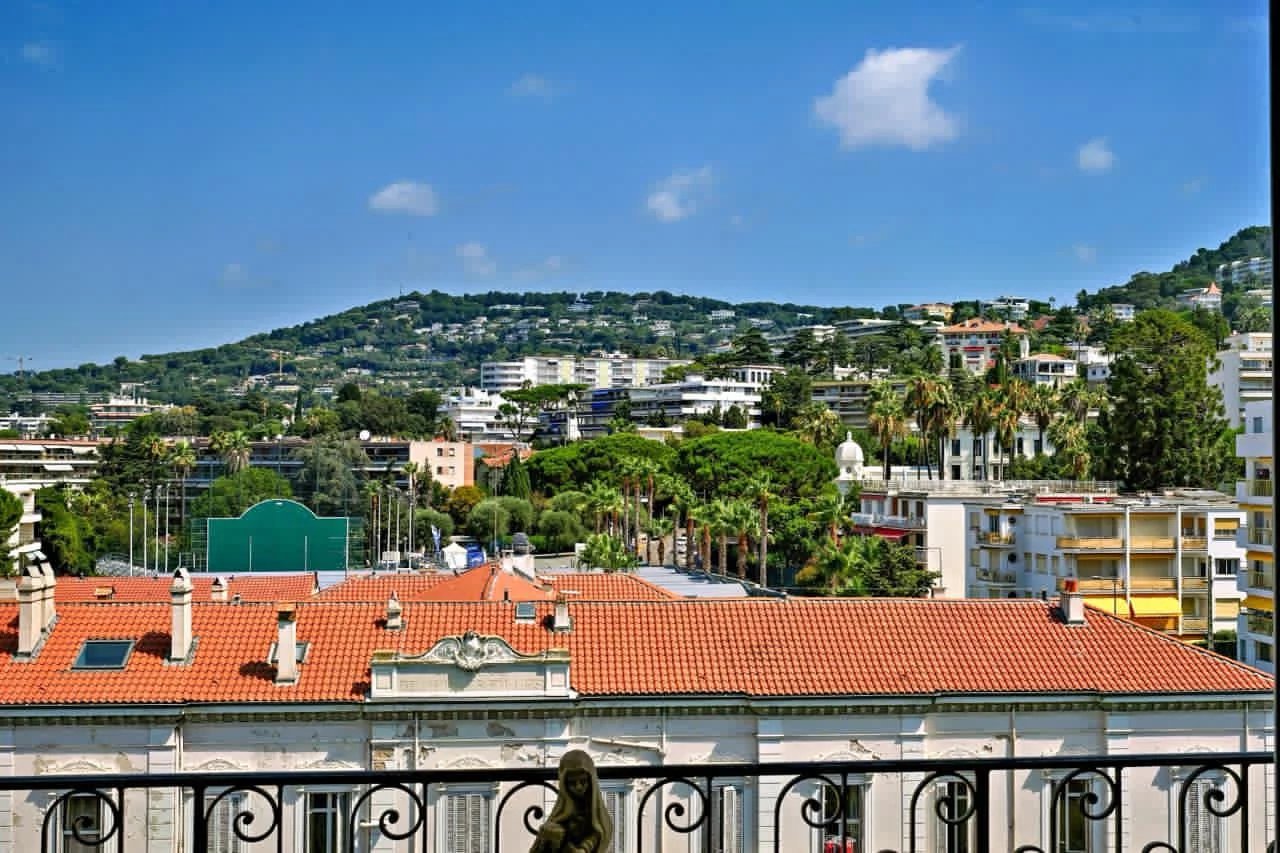 Vue depuis un balcon sur des bâtiments et des collines à Cannes, avec ciel bleu et nuages.