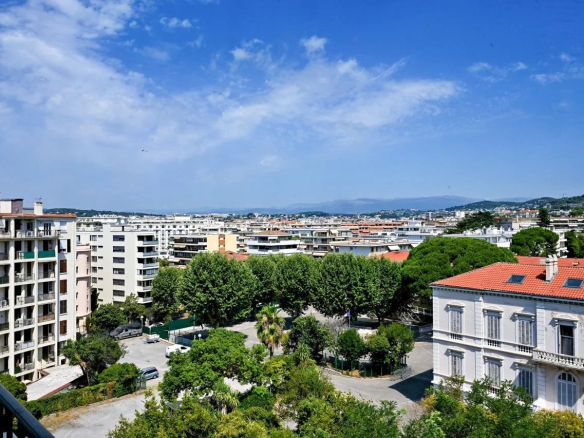 Vue panoramique sur Cannes depuis un appartement bourgeois, avec des bâtiments et des arbres en premier plan.