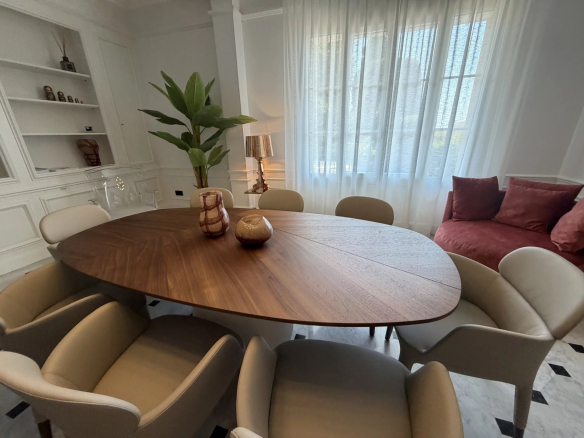 Salle à manger moderne avec une grande table ovale en bois et des chaises claires, lumière naturelle à travers les fenêtres.