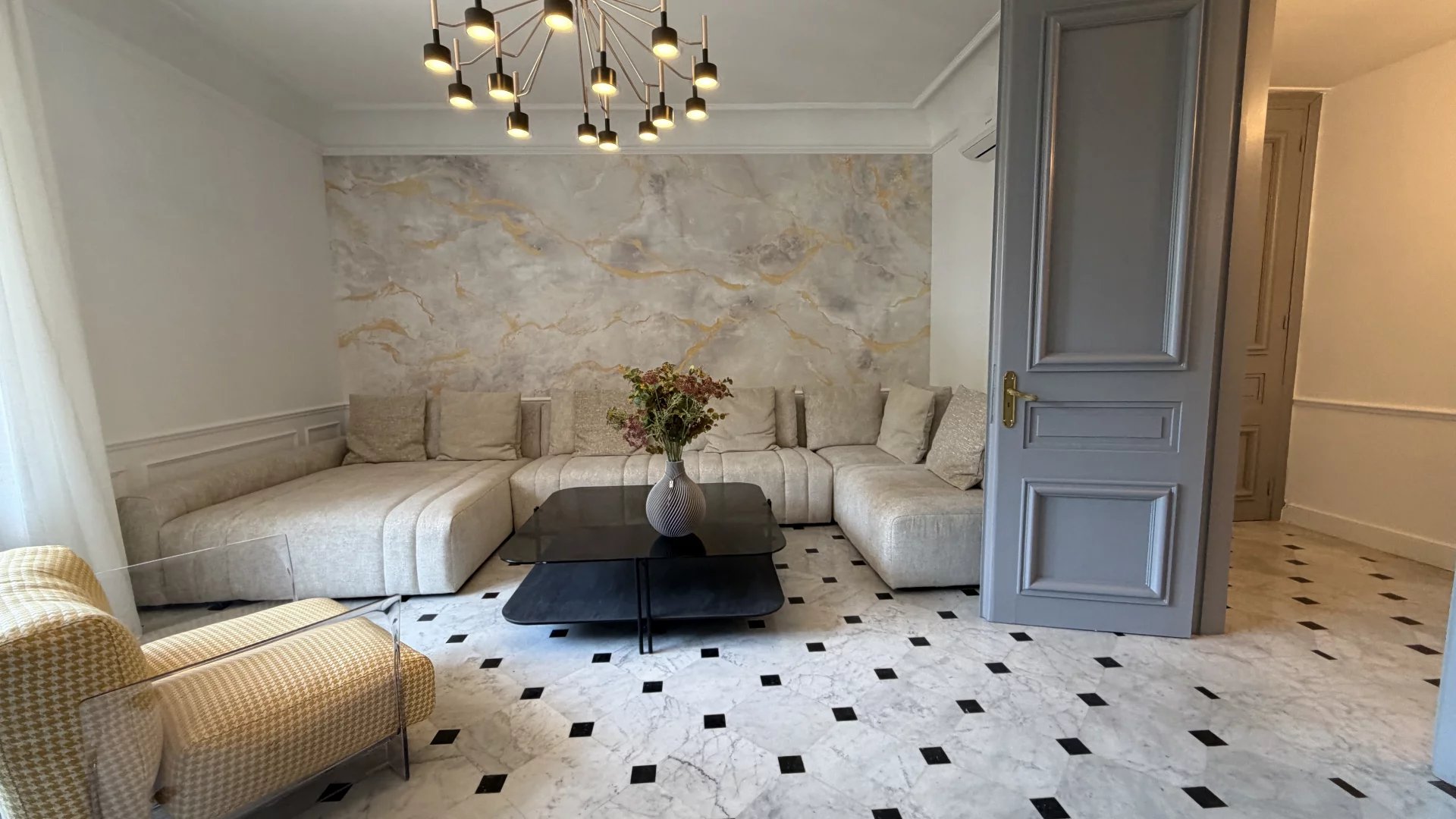 Salon d’un appartement à Cannes Salon spacieux avec canapé moderne et décoration élégante, murs en marbre et sol en carreaux noirs et blancs.