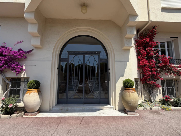 Entrée d'une résidence à Cannes avec des plantes fleuries et une porte en fer forgé.