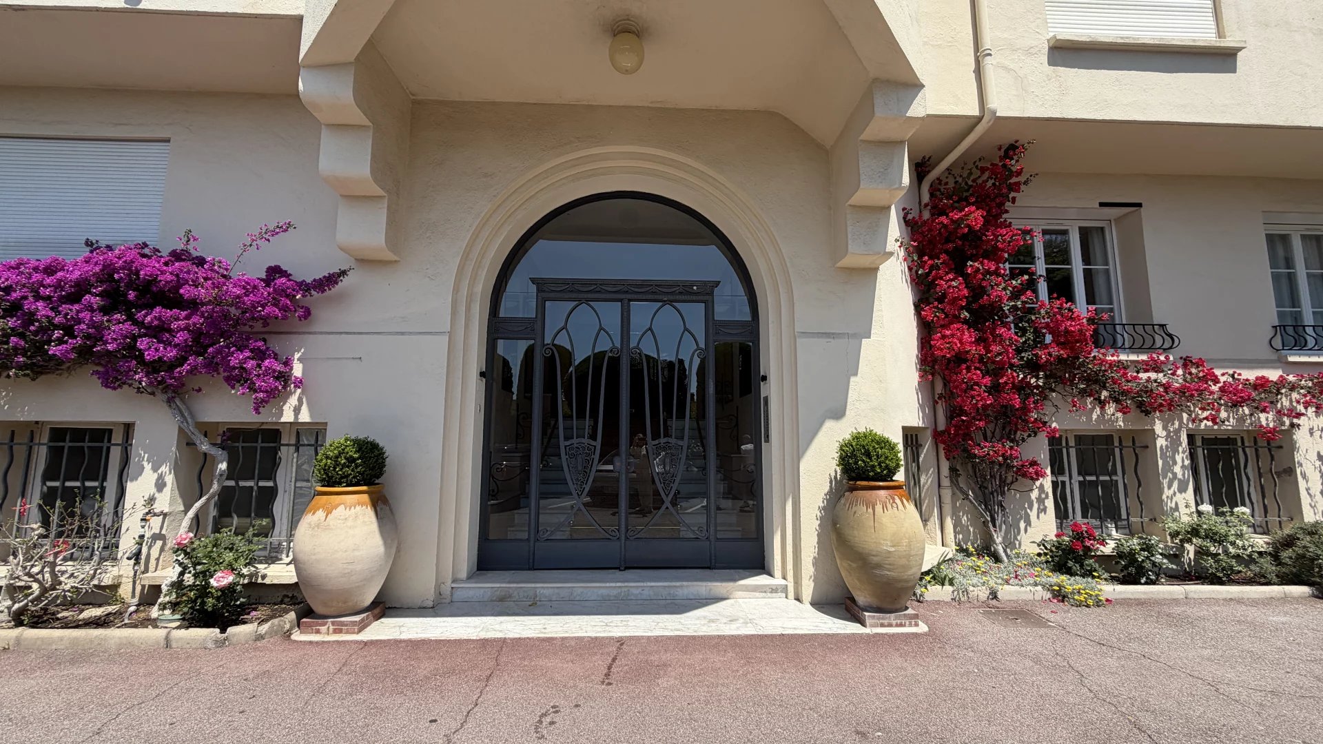 Entrée d’une résidence à Cannes Entrée d'une résidence à Cannes avec des plantes fleuries et une porte en fer forgé.