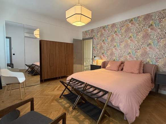 Chambre d'appartement rénové à Cannes avec lit, décor floral et mobilier moderne.