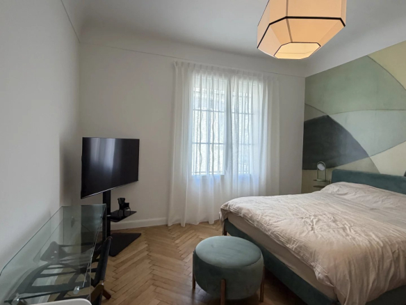 Chambre d'un appartement rénové à Cannes, avec un lit, télévision et fenêtres lumineuses.