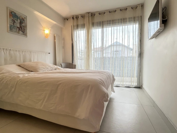 Room in a Cannes apartment with a double bed and a window overlooking a terrace.