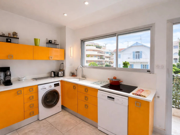 Modern kitchen with orange furniture and appliances, windows overlooking the outside.