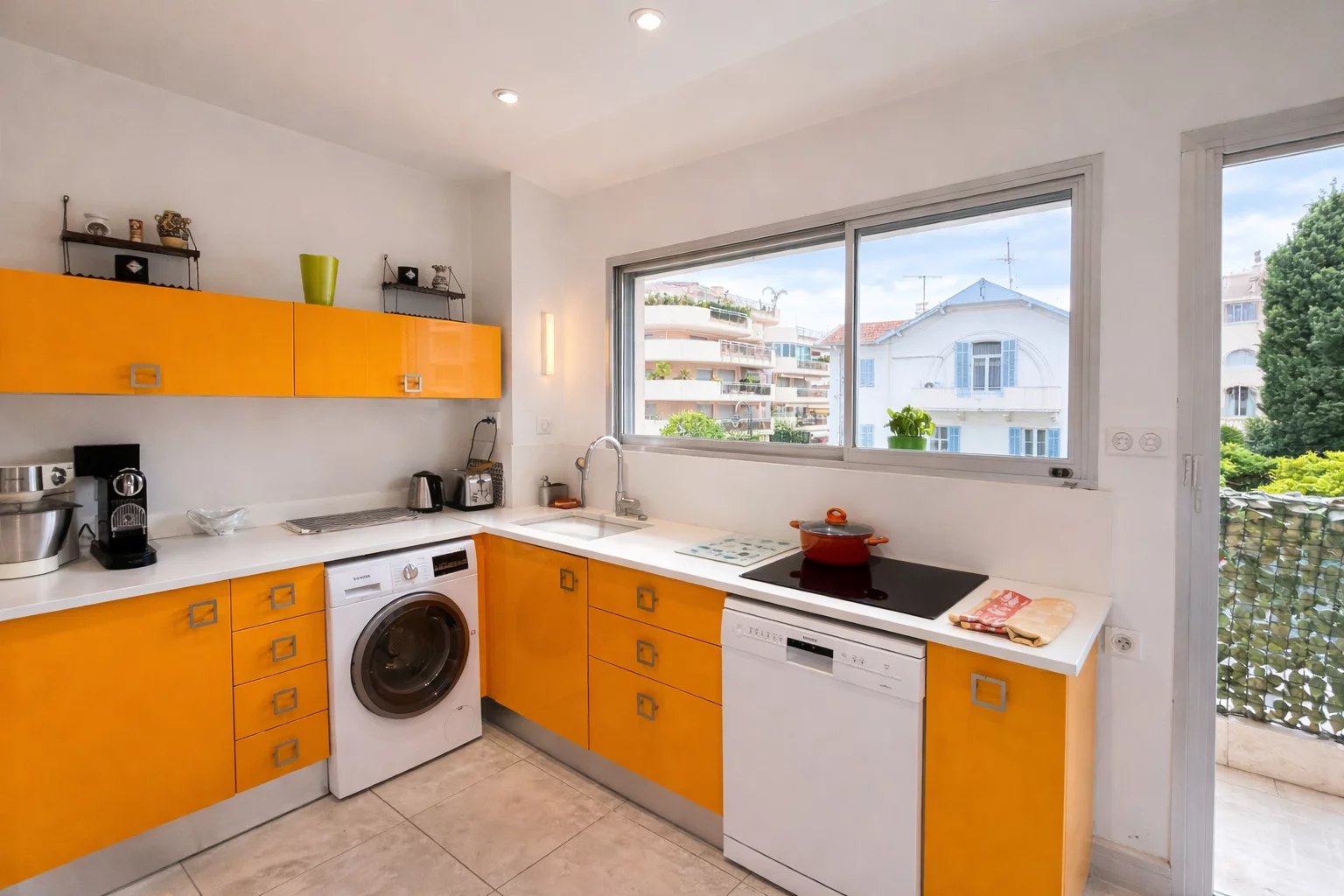 Kitchen of an apartment in Cannes Modern kitchen with orange furniture and appliances, windows overlooking the outside.