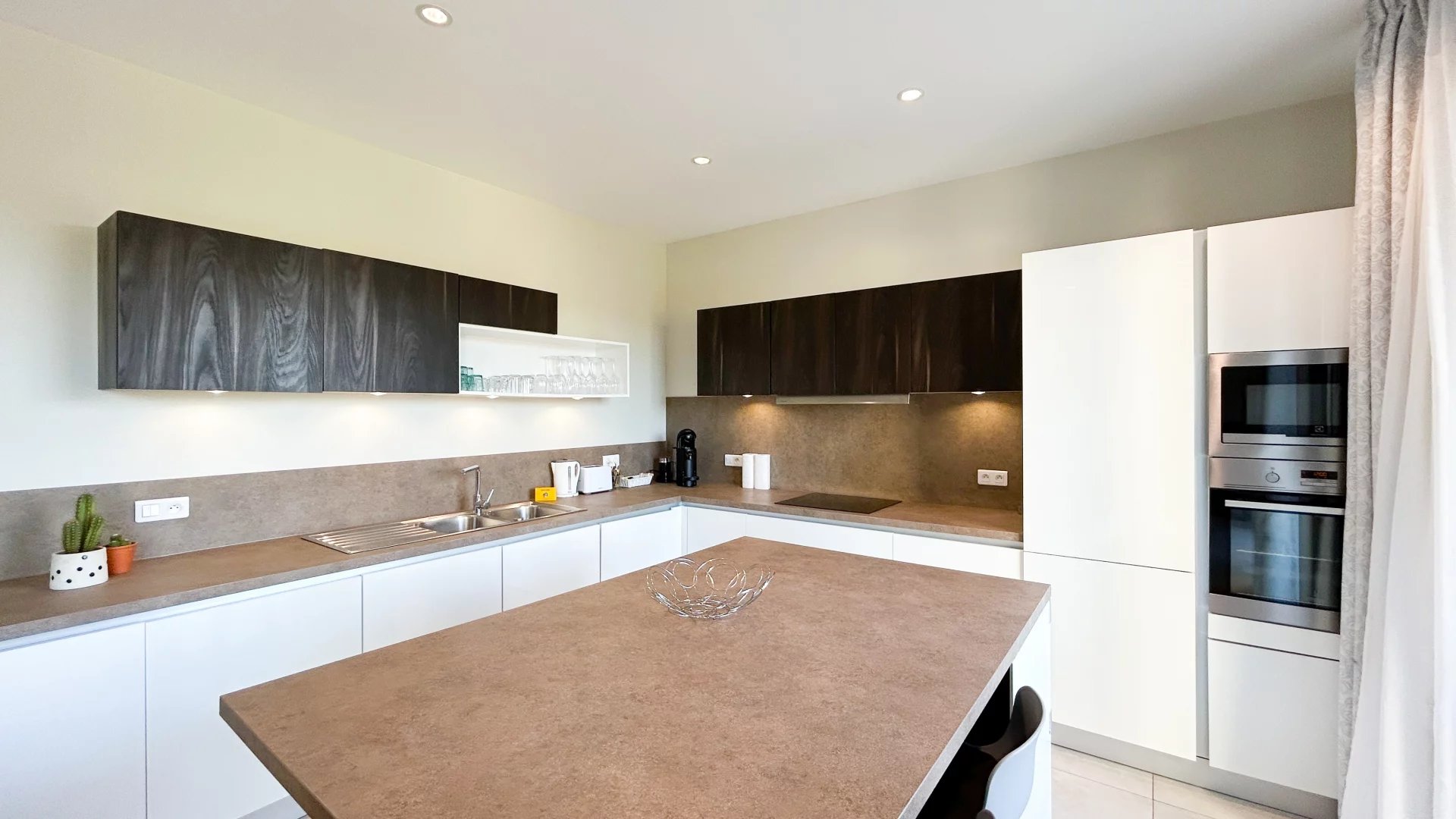 Cuisine d’un appartement à Cannes Cuisine moderne d'un appartement à Cannes avec un îlot central et des meubles en bois et blanc.
